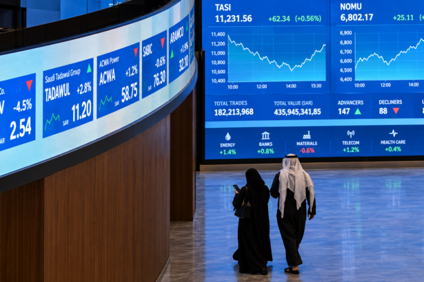 Saudi investors walk past digital market screens at the Tadawul stock exchange in Riyadh