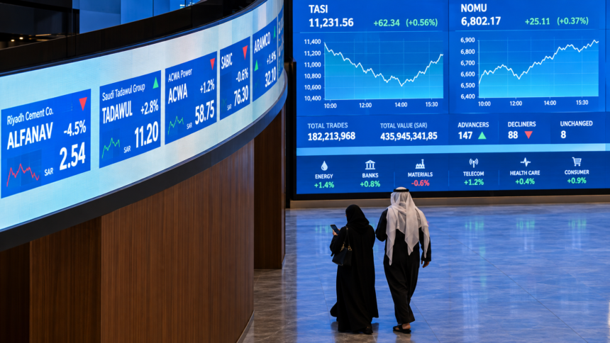 Saudi investors walk past digital market screens at the Tadawul stock exchange in Riyadh