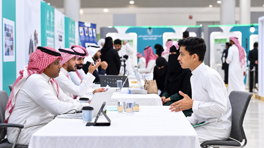 Young Saudi job seeker speaking with recruiters at a career fair